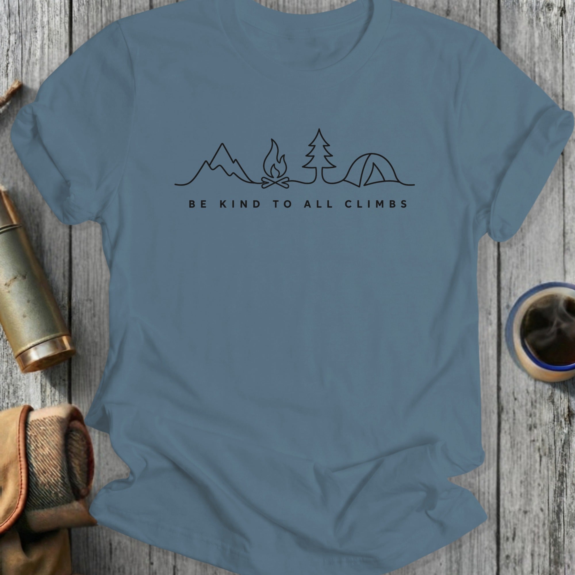 Blue t-shirt with "Be Kind to All Climbs" text and mountain, campfire, tree, tent illustration.
