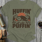Puffin wearing a crown with "Huffin' Puffin'" text, sunset and mountains background.