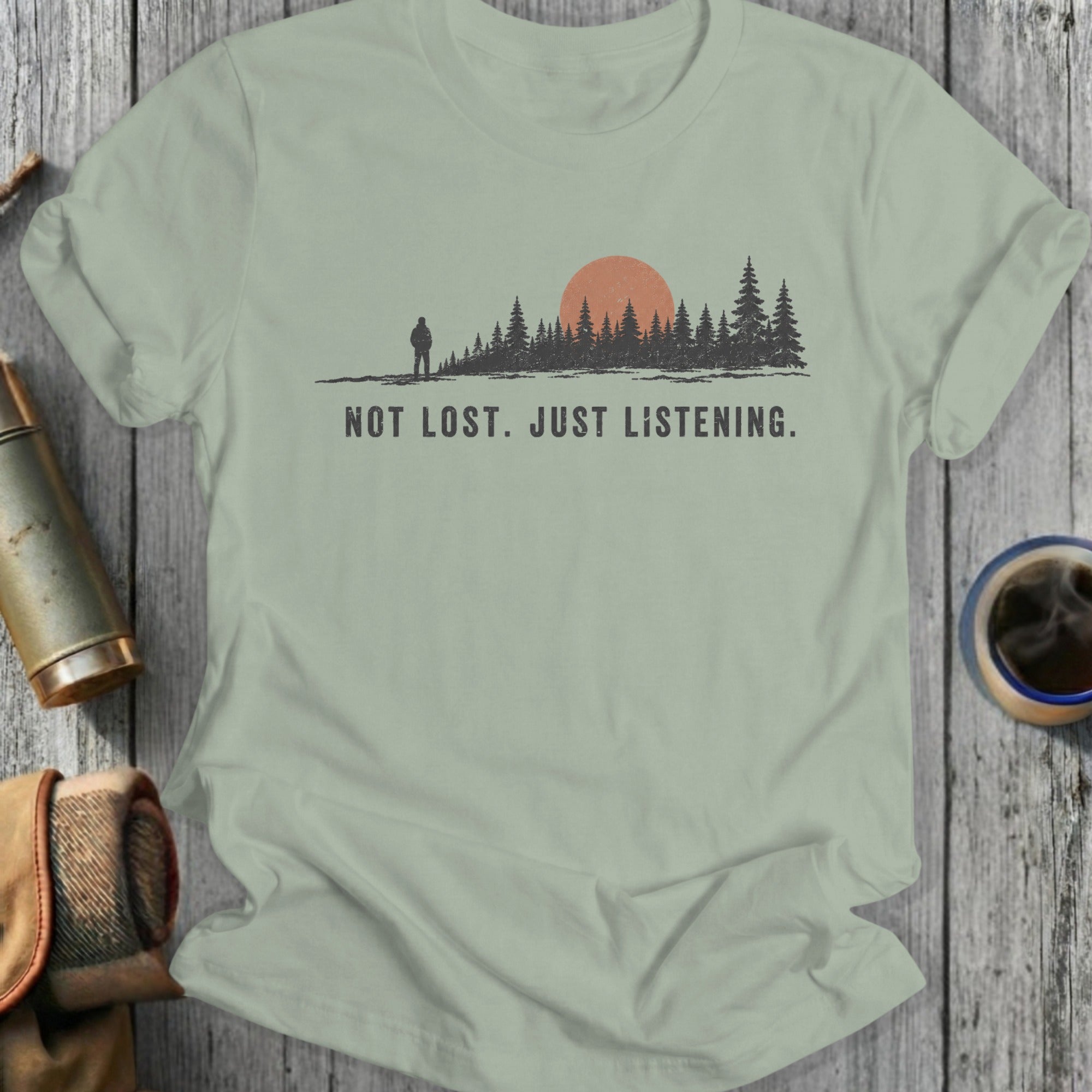 T-shirt with "NOT LOST. JUST LISTENING." text over a forest silhouette and sun.