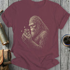 Bigfoot holding a jar of fireflies on a maroon t-shirt.