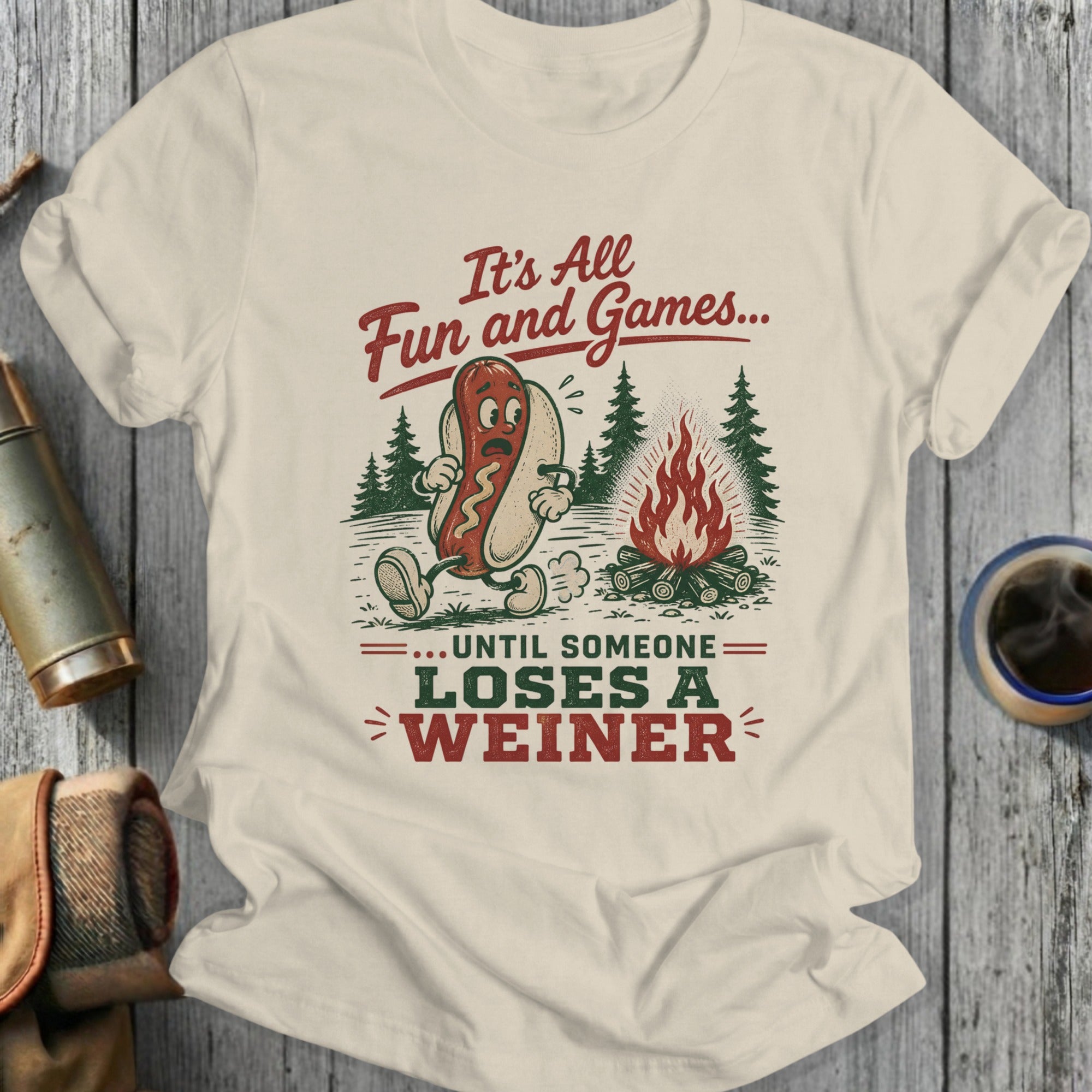 T-shirt with a hot dog around a campfire, reading "It's All Fun and Games... Until Someone Loses A Weiner."