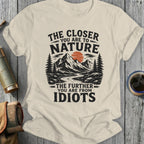Cream t-shirt with "The Closer You Are To Nature The Further You Are From Idiots" text and mountain graphic.