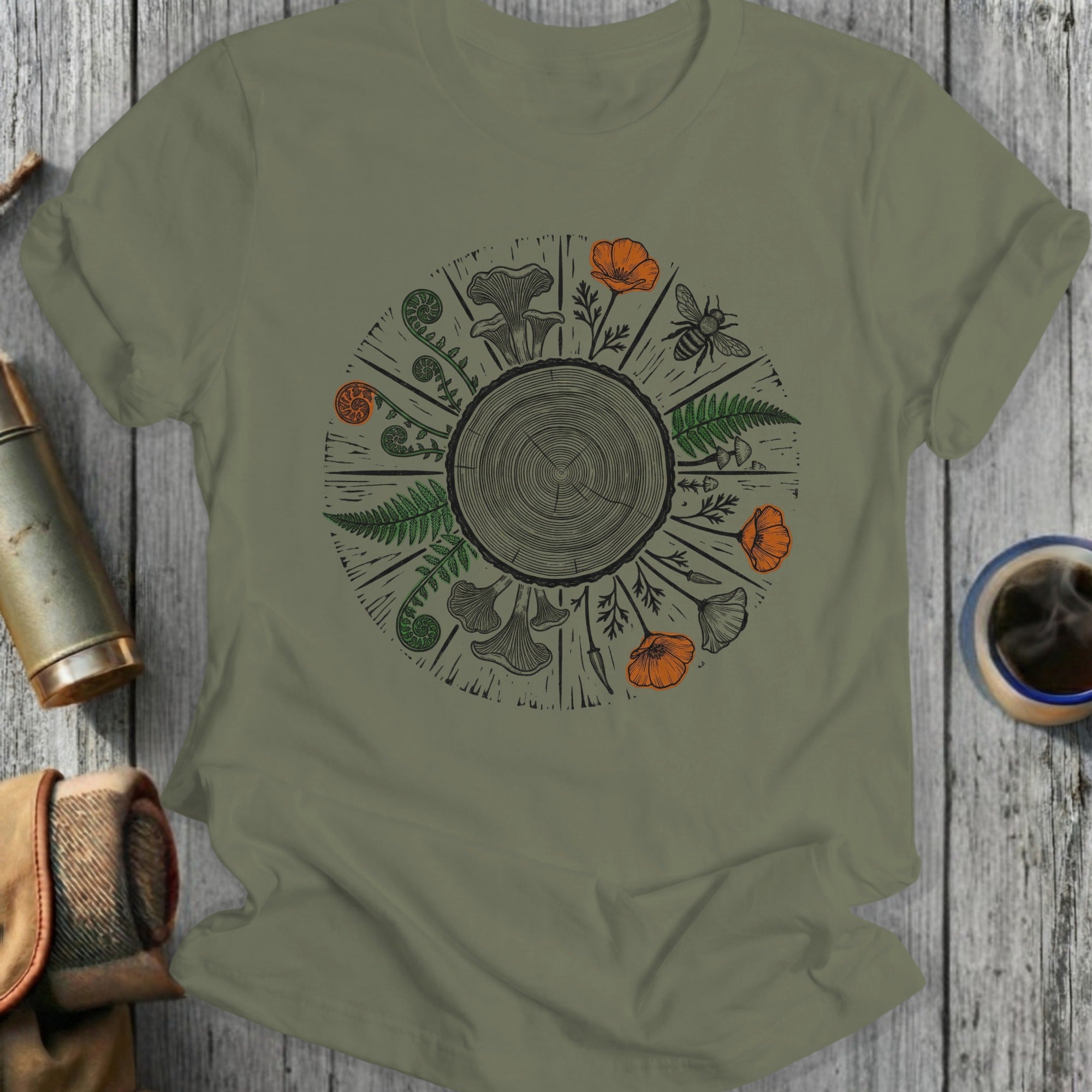 Olive green t-shirt with circular botanical design featuring mushrooms, ferns, and flowers.