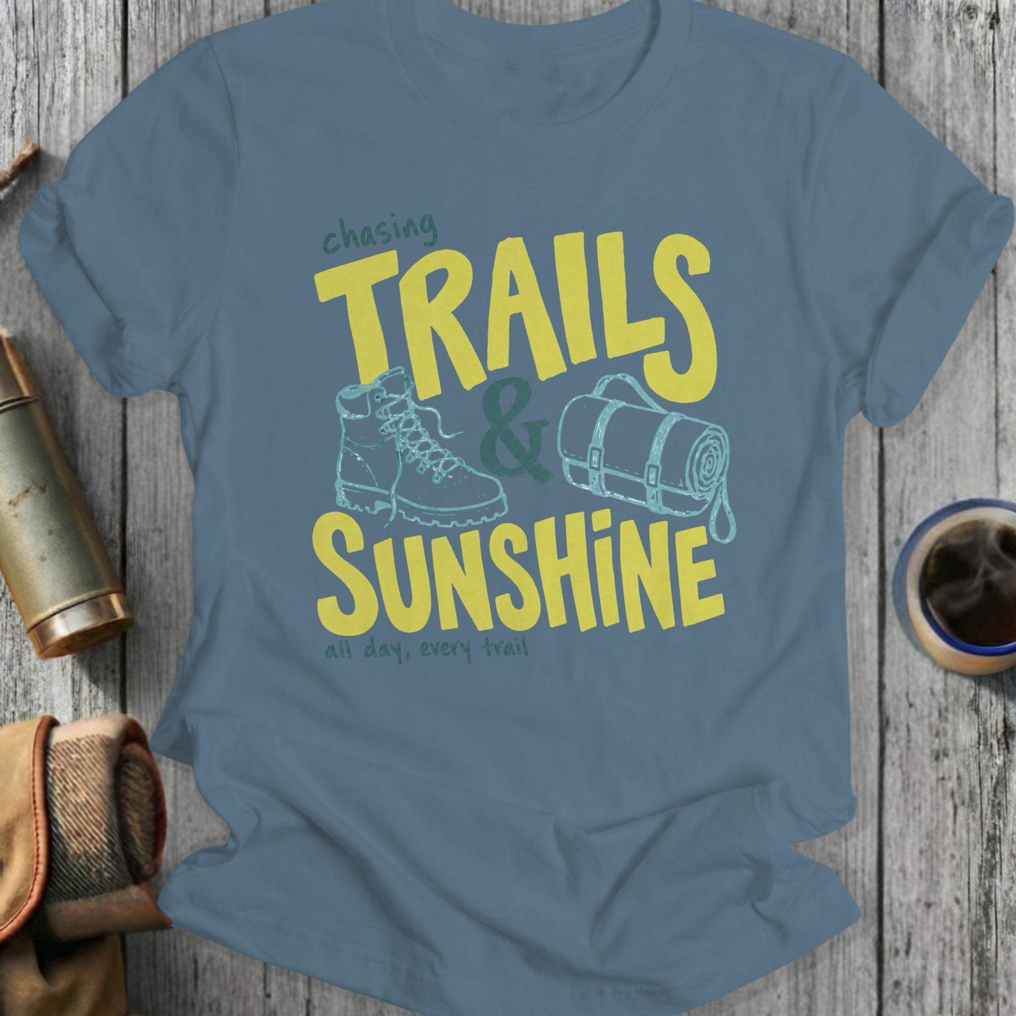 Blue t-shirt with "Chasing Trails & Sunshine" text, hiking boot, and rolled sleeping bag graphic.