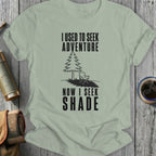 Light green t-shirt with black text "I USED TO SEEK ADVENTURE NOW I SEEK SHADE" and a graphic.