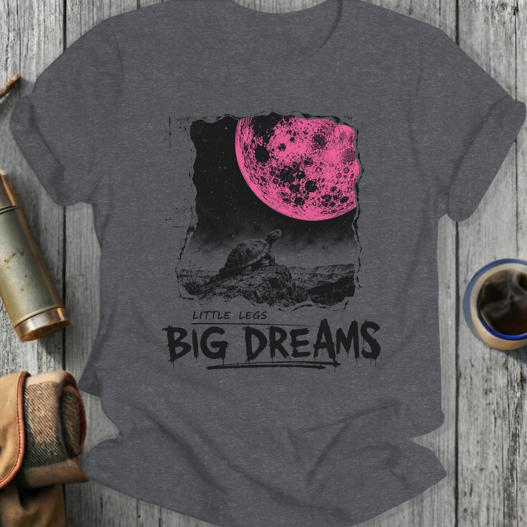 Dark t-shirt with graphic of a turtle looking at a large pink moon, text reads "LITTLE LEGS BIG DREAMS".