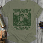 Frog wearing a hat in the woods, text reads "Things disappear in the woods. Maybe a sock. Maybe you."