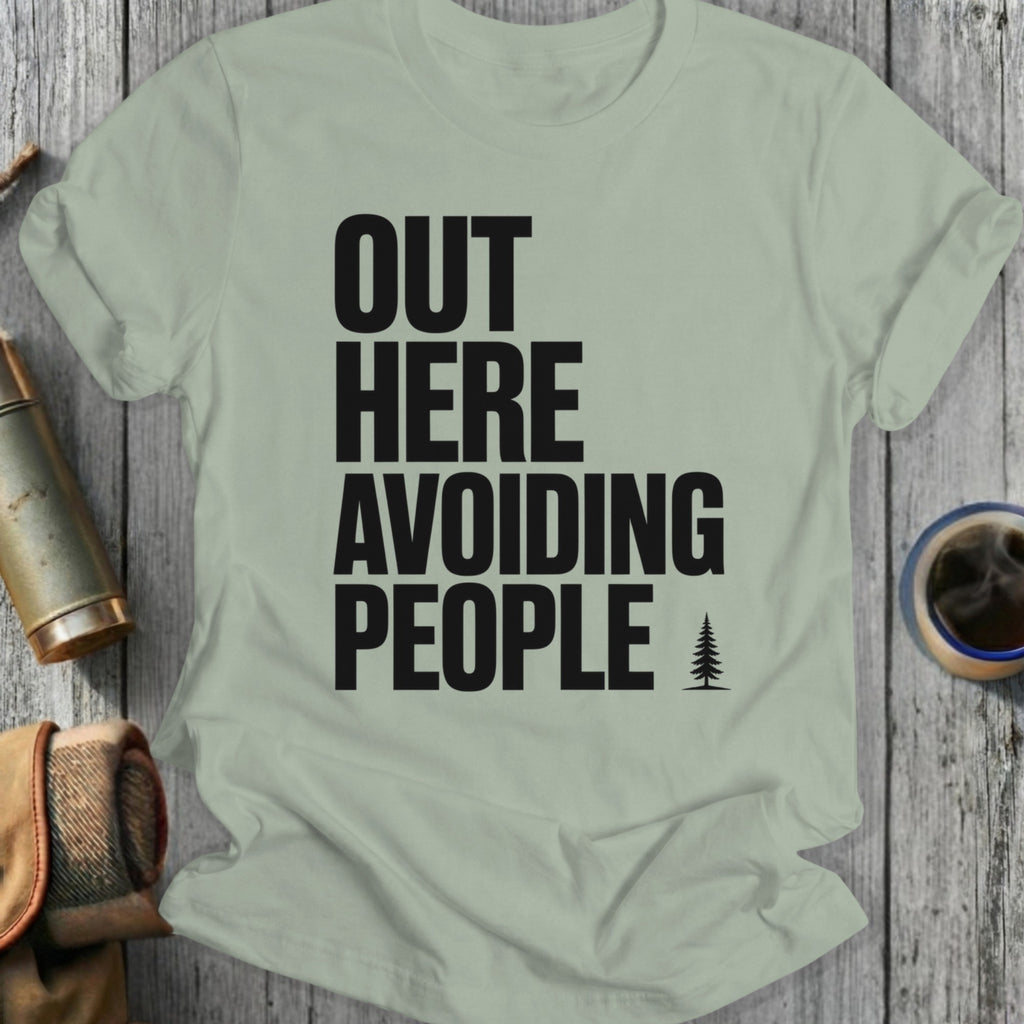 Light green t-shirt with bold black text "OUT HERE AVOIDING PEOPLE" and a small pine tree icon.