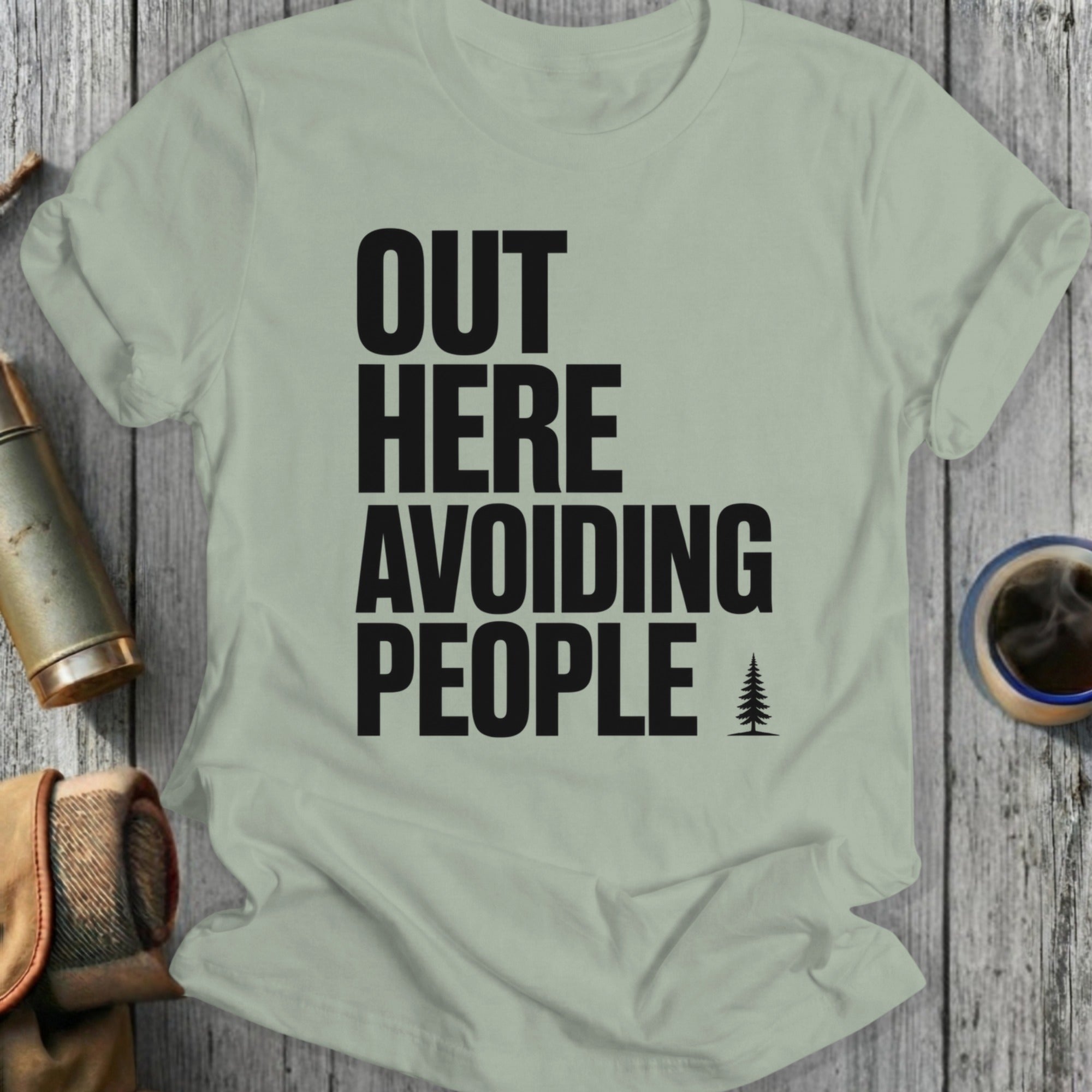 Light green t-shirt with bold black text "OUT HERE AVOIDING PEOPLE" and a small pine tree icon.
