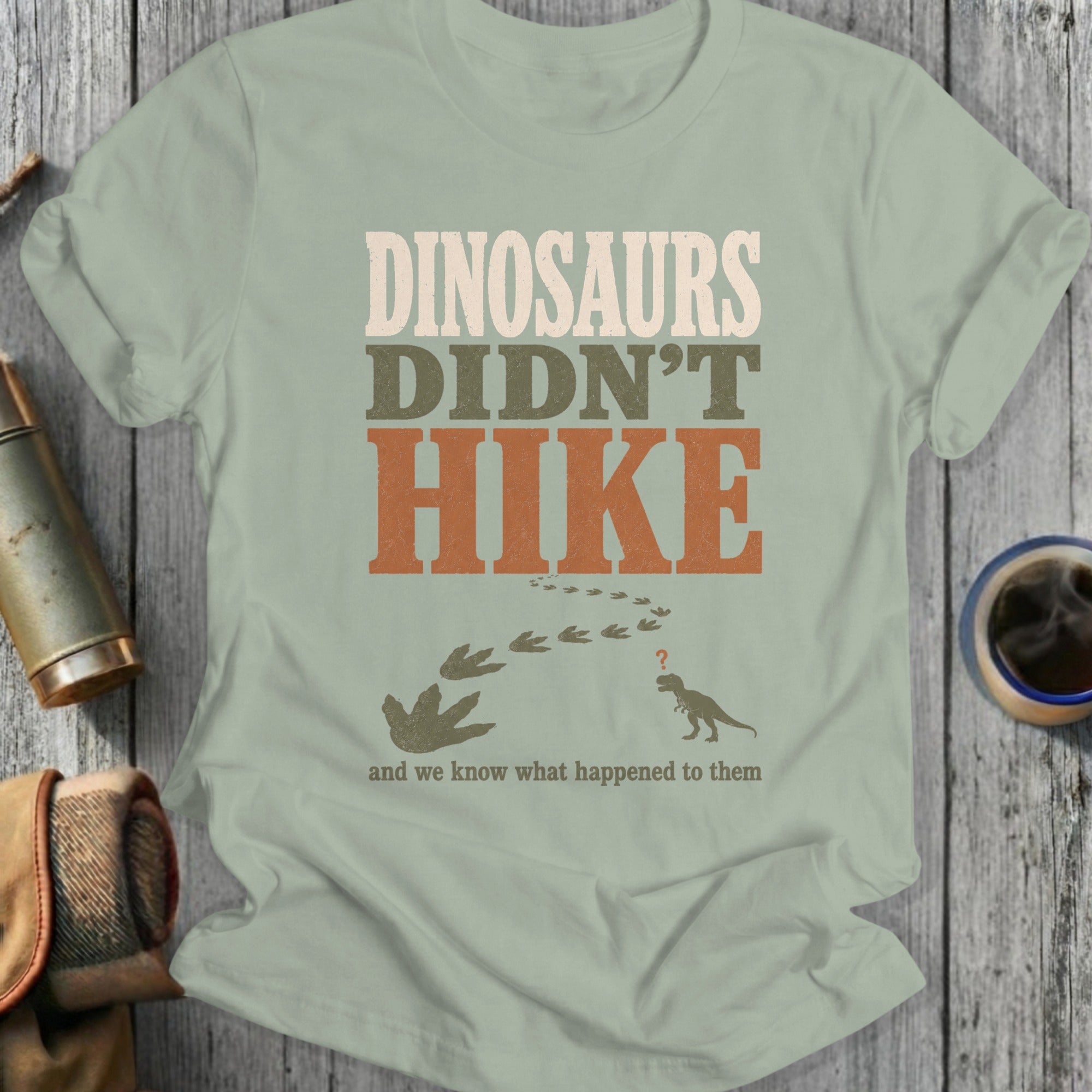 T-shirt with text "DINOSAURS DIDN'T HIKE" and dinosaur tracks and silhouette.