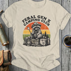 Feral Gen X Camping Club raccoon with marshmallow, vintage sunset, and camping gear.