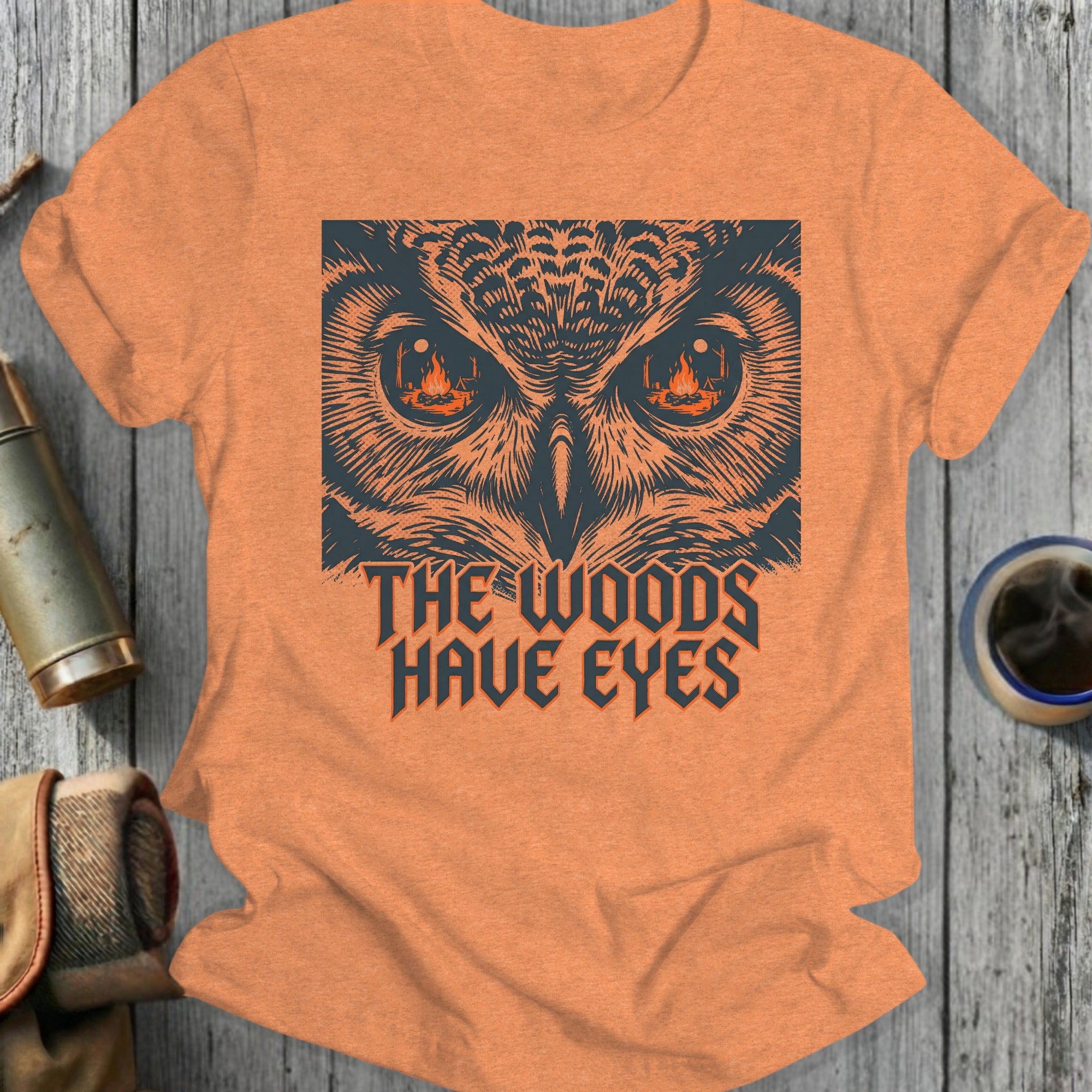 Orange t-shirt with graphic of owl eyes and text "The Woods Have Eyes".