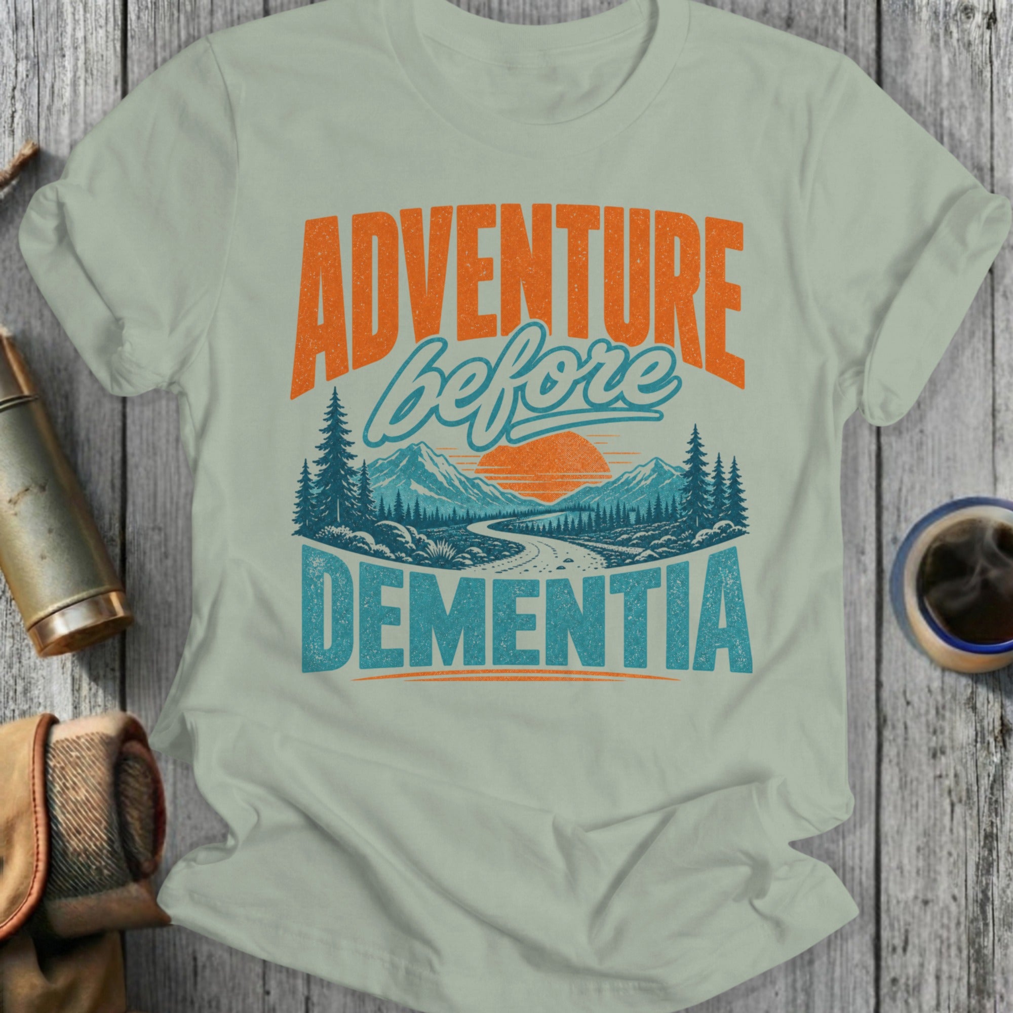 Light green t-shirt with "ADVENTURE before DEMENTIA" and mountains graphic.