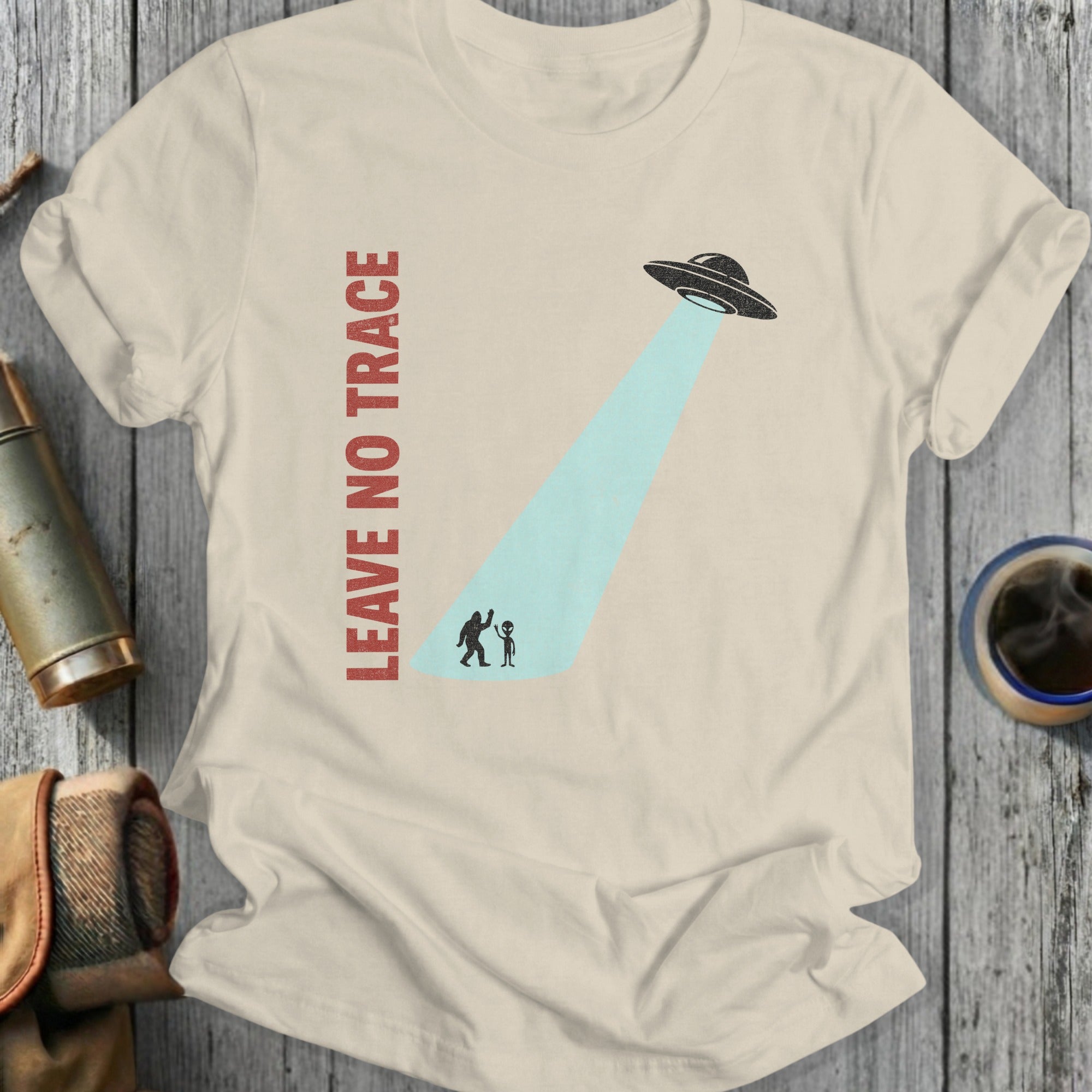 Cream t-shirt with "LEAVE NO TRACE" and Bigfoot being abducted by a UFO.