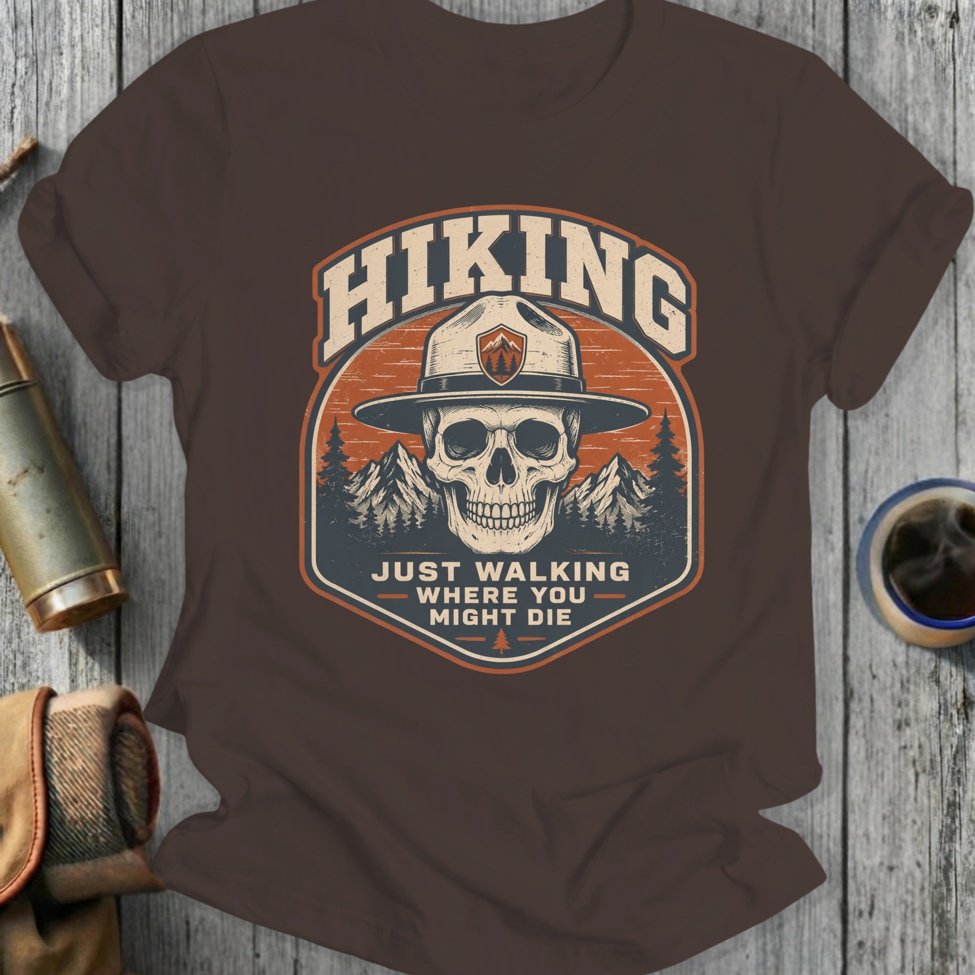 Brown t-shirt with skull, mountains, and text "Hiking Just Walking Where You Might Die".