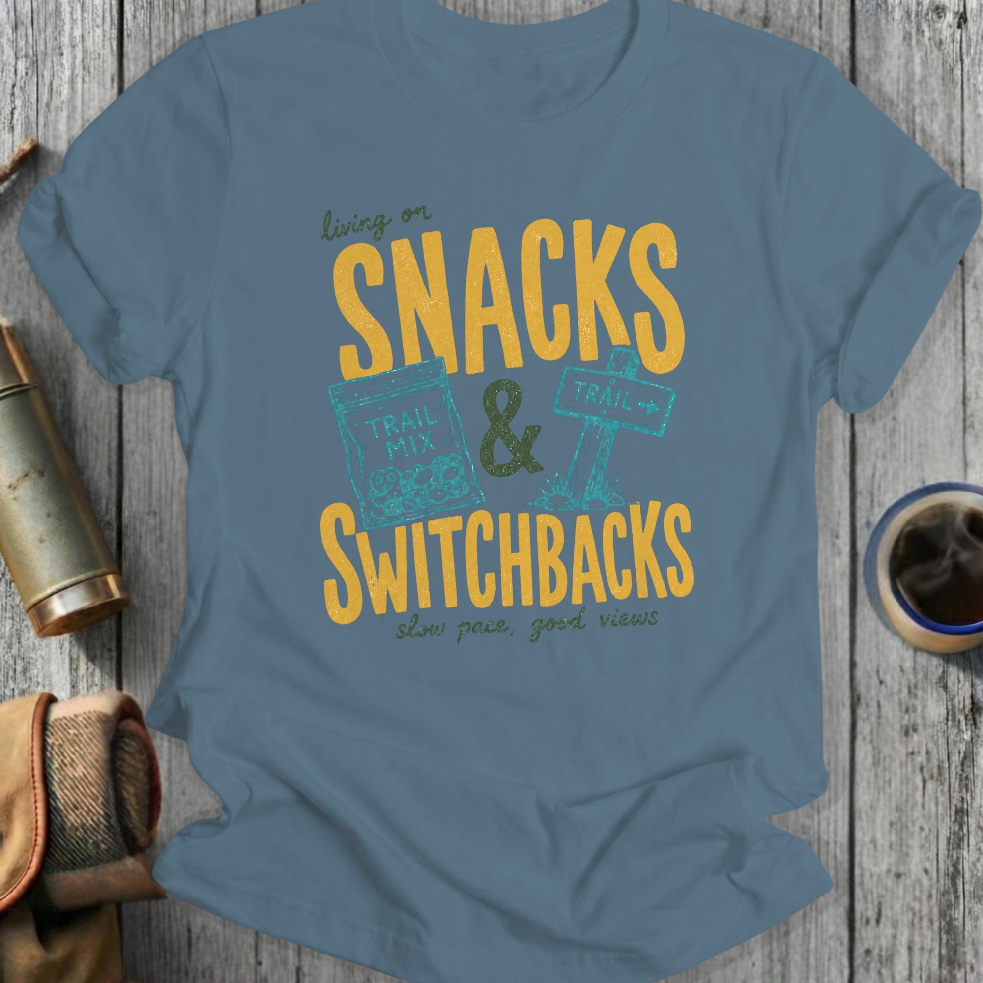 Blue t-shirt graphic with "living on SNACKS & SWITCHBACKS, slow pace, good views".