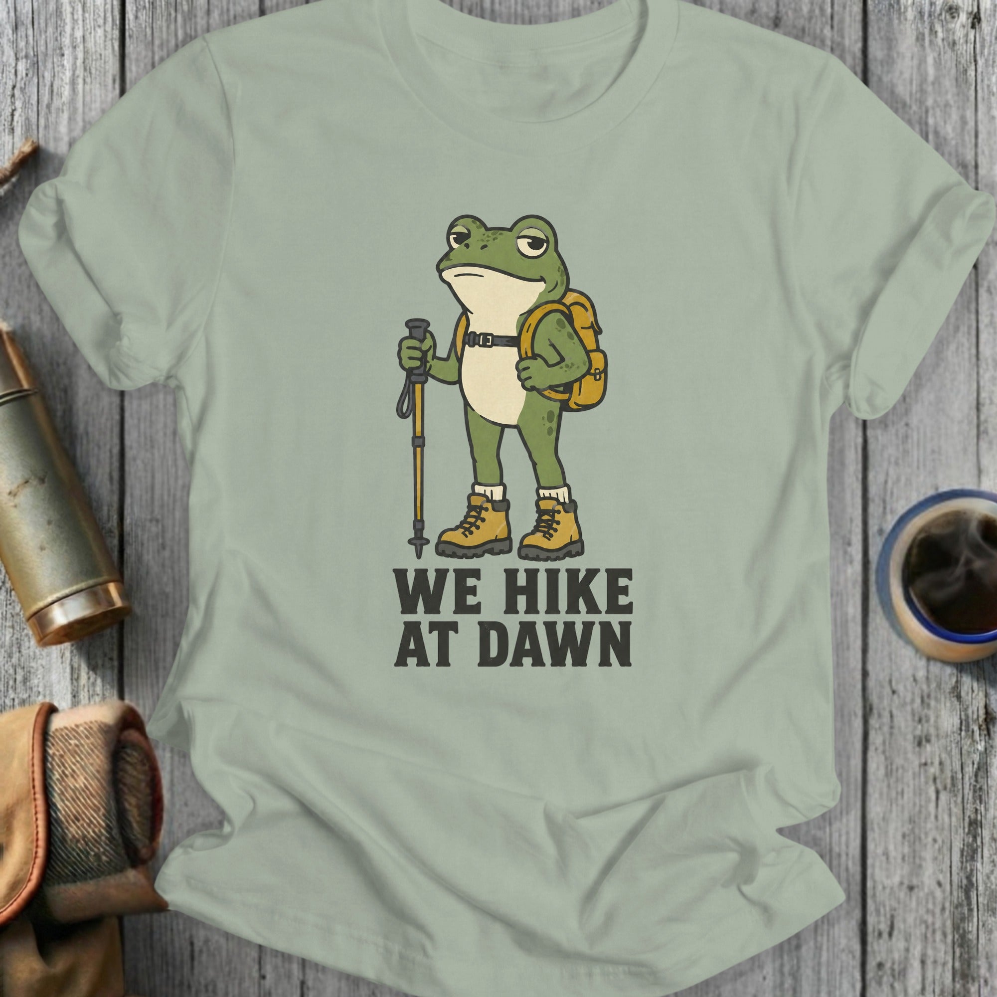 Cartoon frog with backpack and hiking pole, text "WE HIKE AT DAWN".