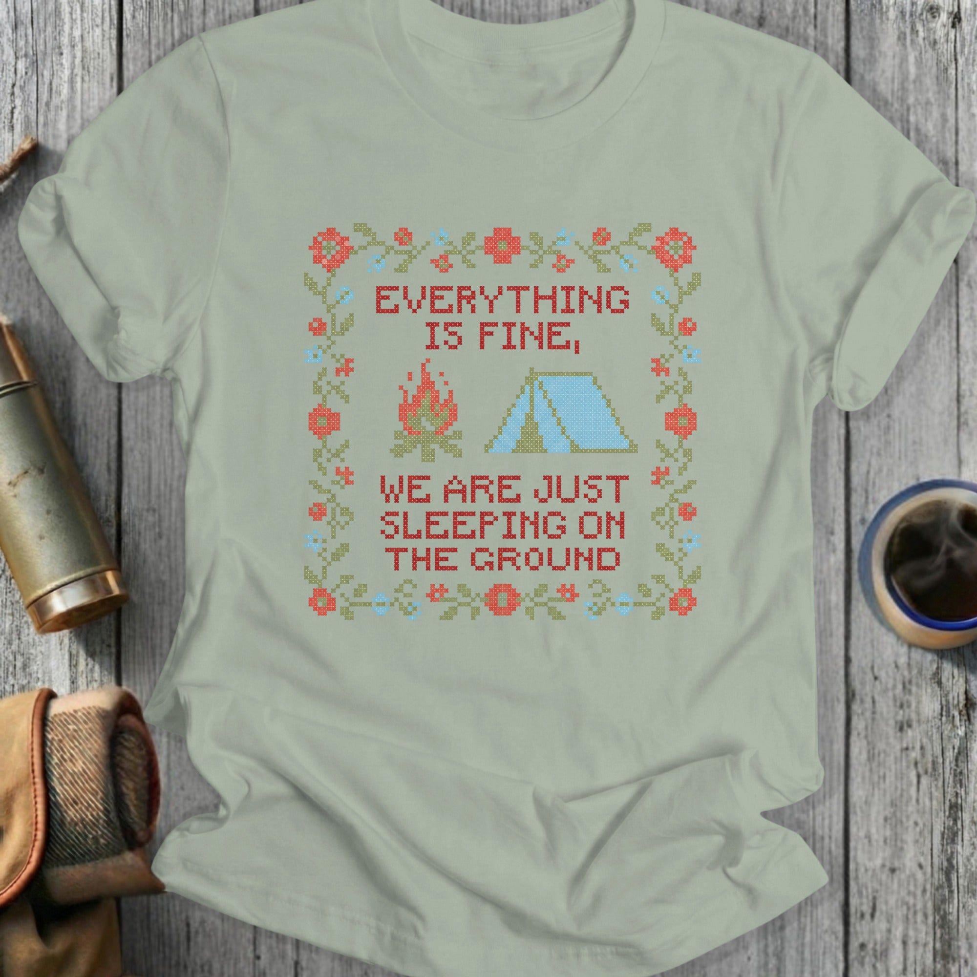 T-shirt with cross-stitch design: "Everything is fine, we are just sleeping on the ground."