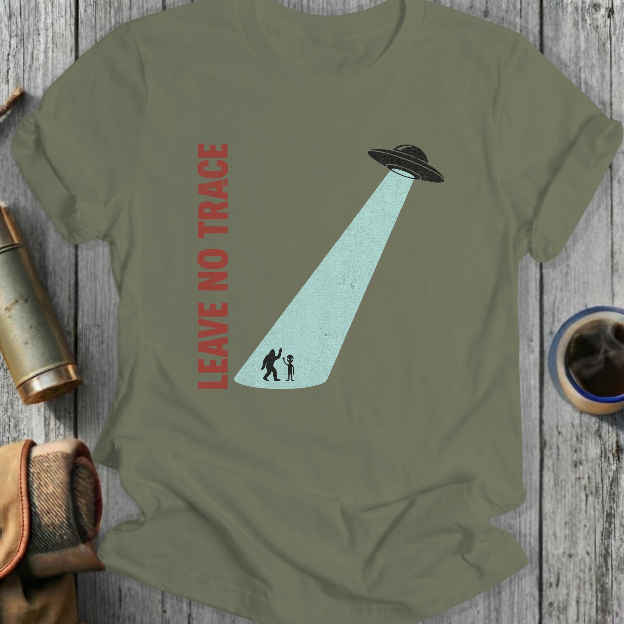 Olive green t-shirt with UFO beam abducting two small figures and "LEAVE NO TRACE" text.