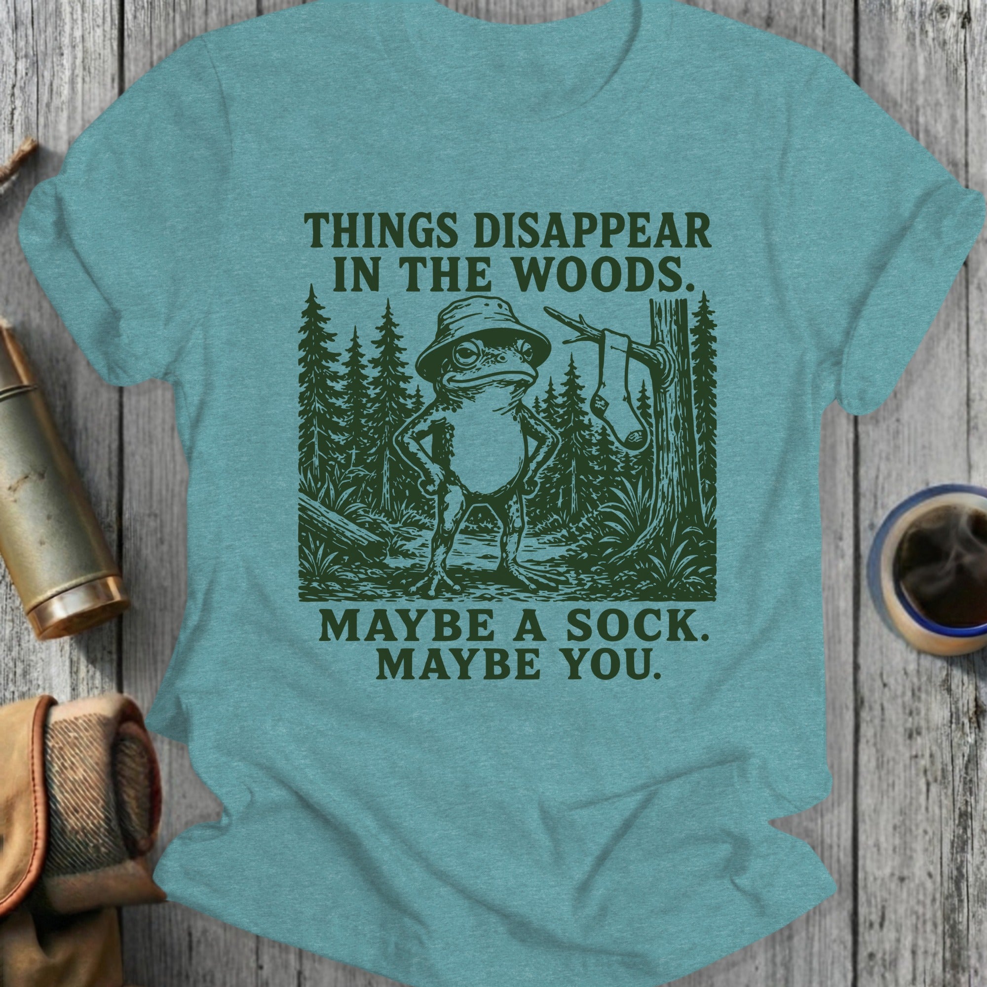 T-shirt with a frog in a hat and text "THINGS DISAPPEAR IN THE WOODS. MAYBE A SOCK. MAYBE YOU."