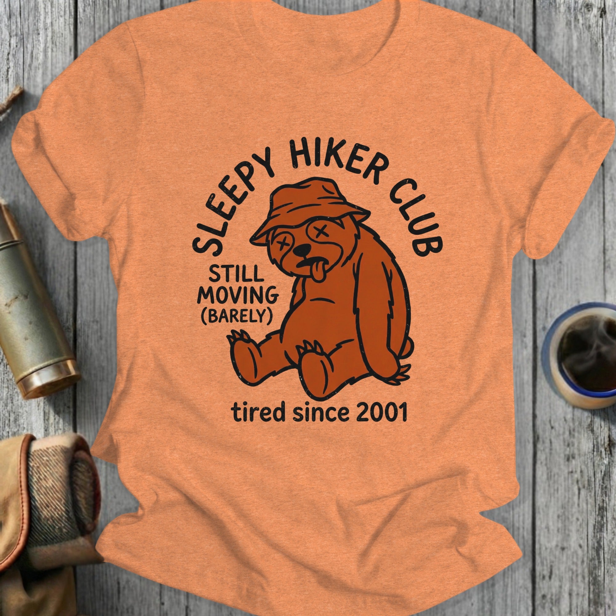 T-shirt graphic: tired bear wearing hat, "Sleepy Hiker Club", "Still Moving (Barely)", "tired since 2001".