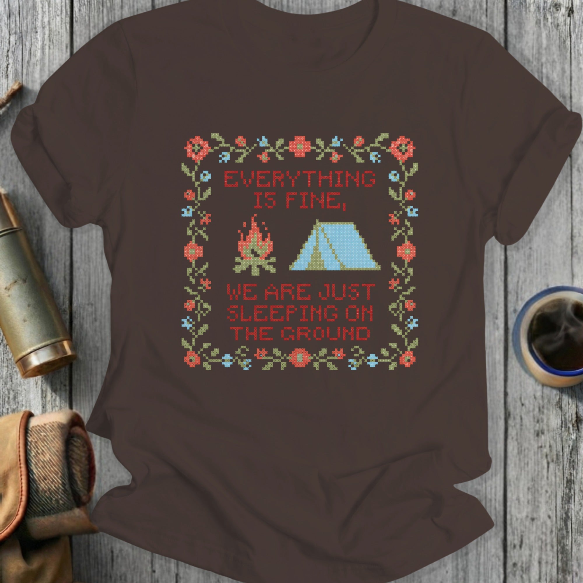Brown t-shirt with floral border, tent, and campfire graphic with text.