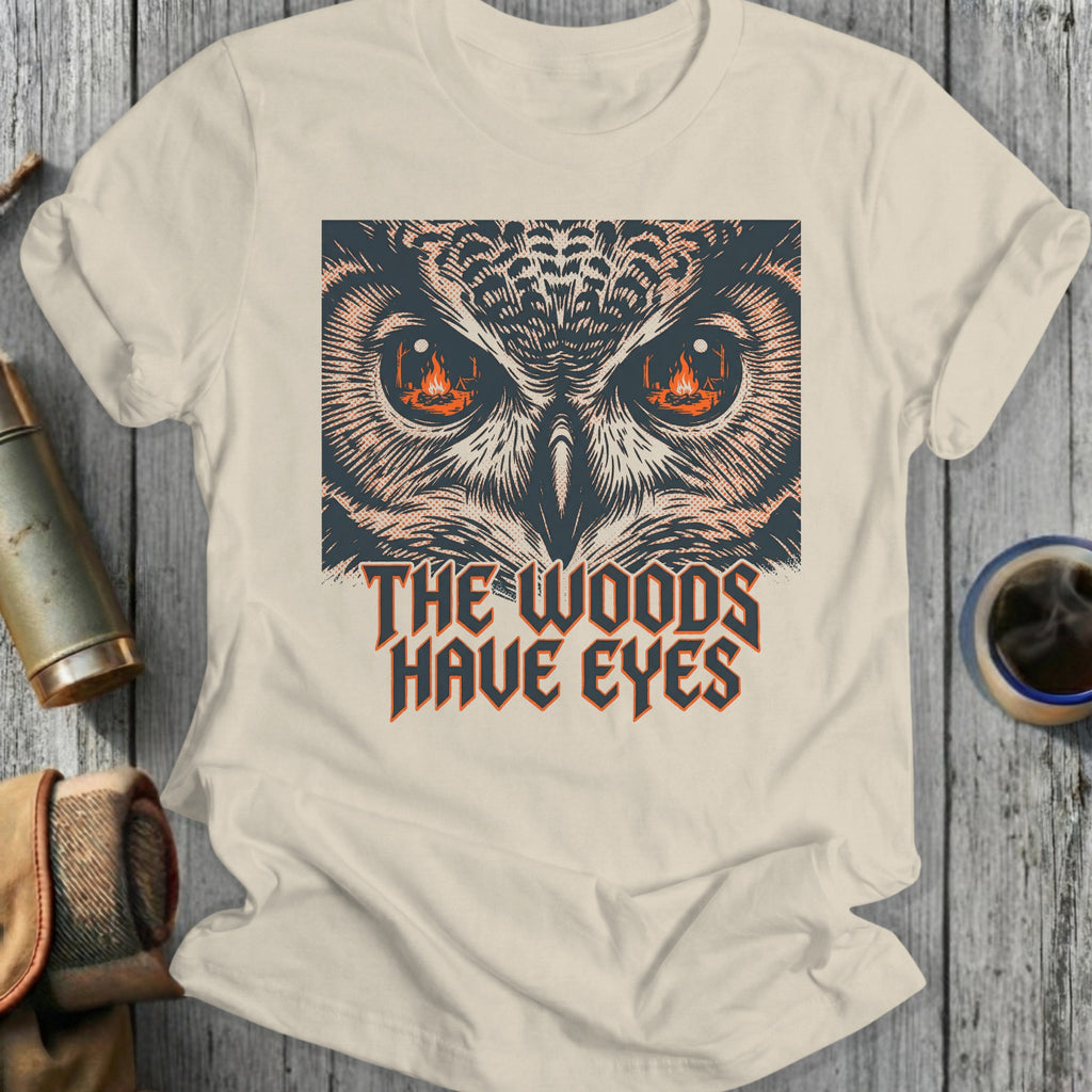 T-shirt graphic featuring an owl's face with fiery eyes and text reading "The Woods Have Eyes."