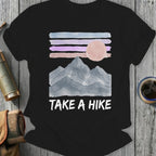Black t-shirt with watercolor mountains, sun, and "TAKE A HIKE" text.