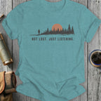 Teal t-shirt featuring a silhouette of a person and pine trees with an orange sun and text "NOT LOST. JUST LISTENING."