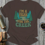 Brown t-shirt with "I'M A FREAK FOR THE CREEK" text and forest graphic.
