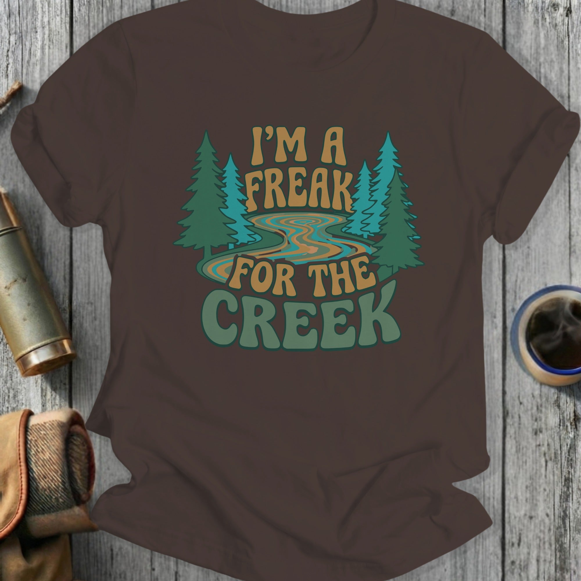 Brown t-shirt with "I'M A FREAK FOR THE CREEK" text and forest graphic.