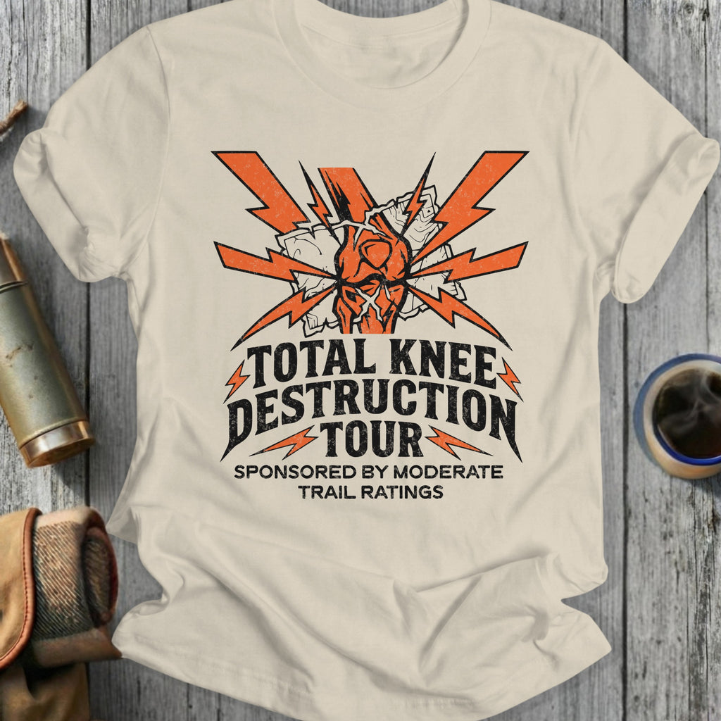 Beige t-shirt with 'Total Knee Destruction Tour' graphic design on a wooden surface.