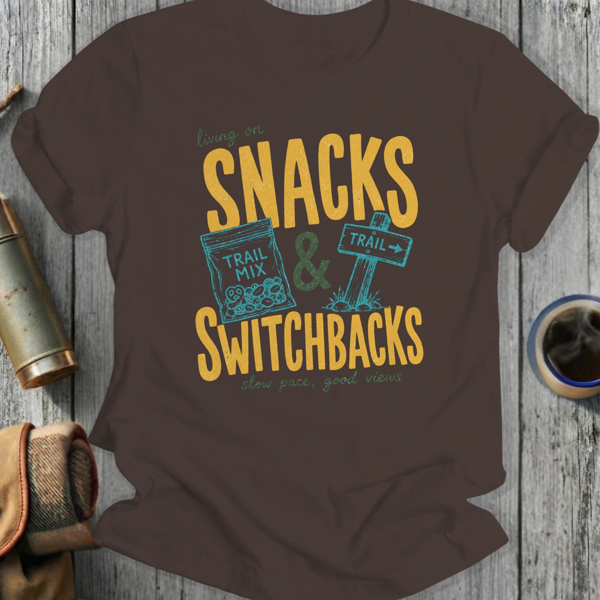 Brown t-shirt with graphic saying "Living on Snacks & Switchbacks" and "slow pace, good views".