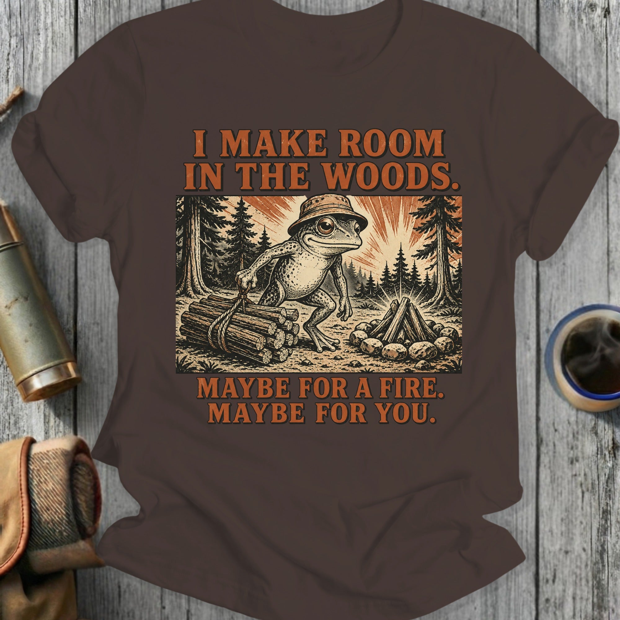 Frog wearing hat in woods, holding logs, with text "I MAKE ROOM IN THE WOODS. MAYBE FOR A FIRE. MAYBE FOR YOU."