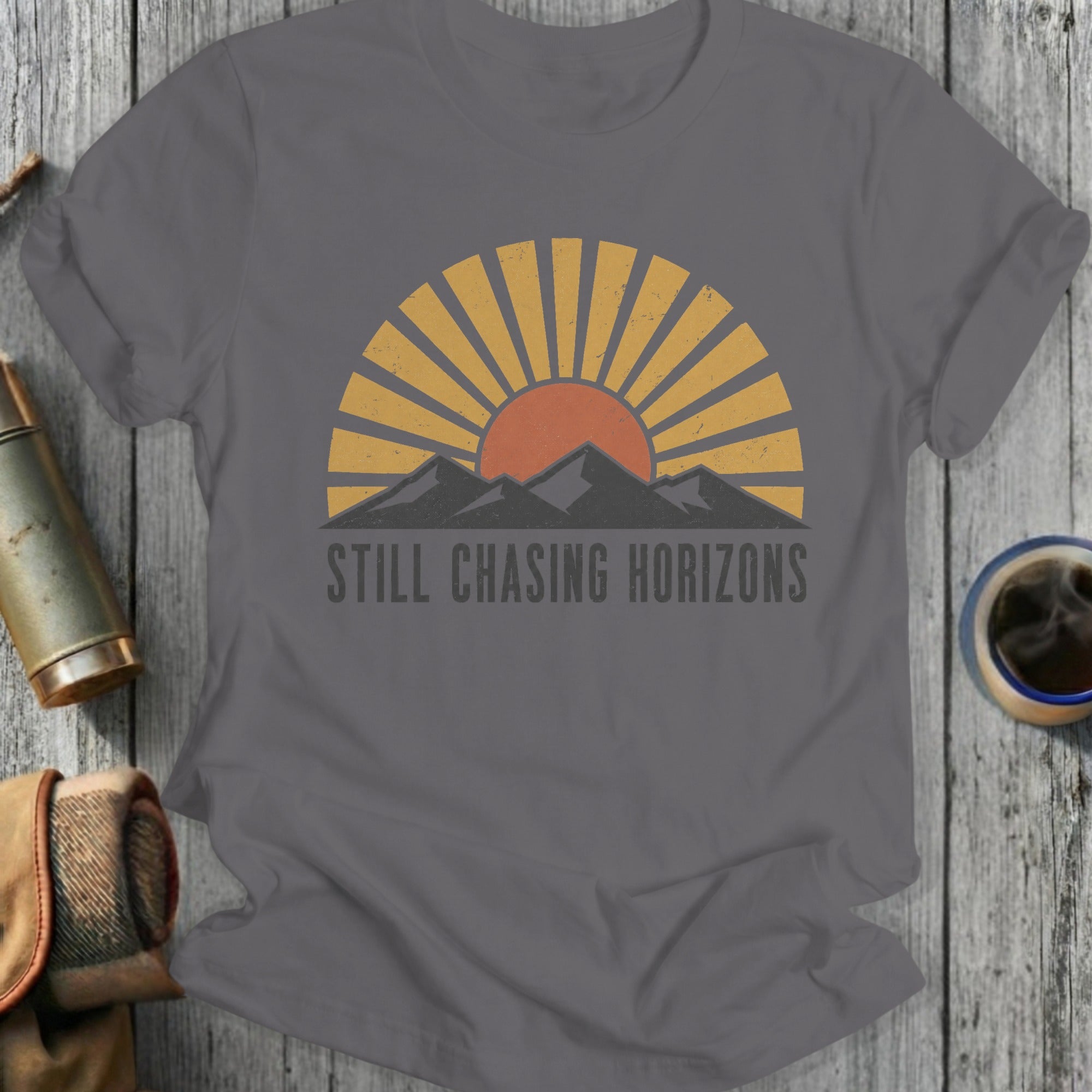 Grey t-shirt with sun, mountains, and "STILL CHASING HORIZONS" text.