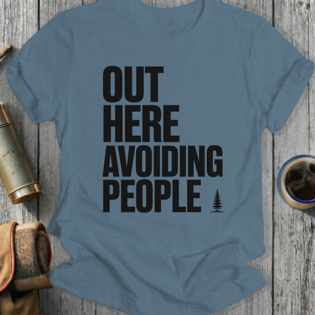 Blue t-shirt with black text "OUT HERE AVOIDING PEOPLE" and a small pine tree.