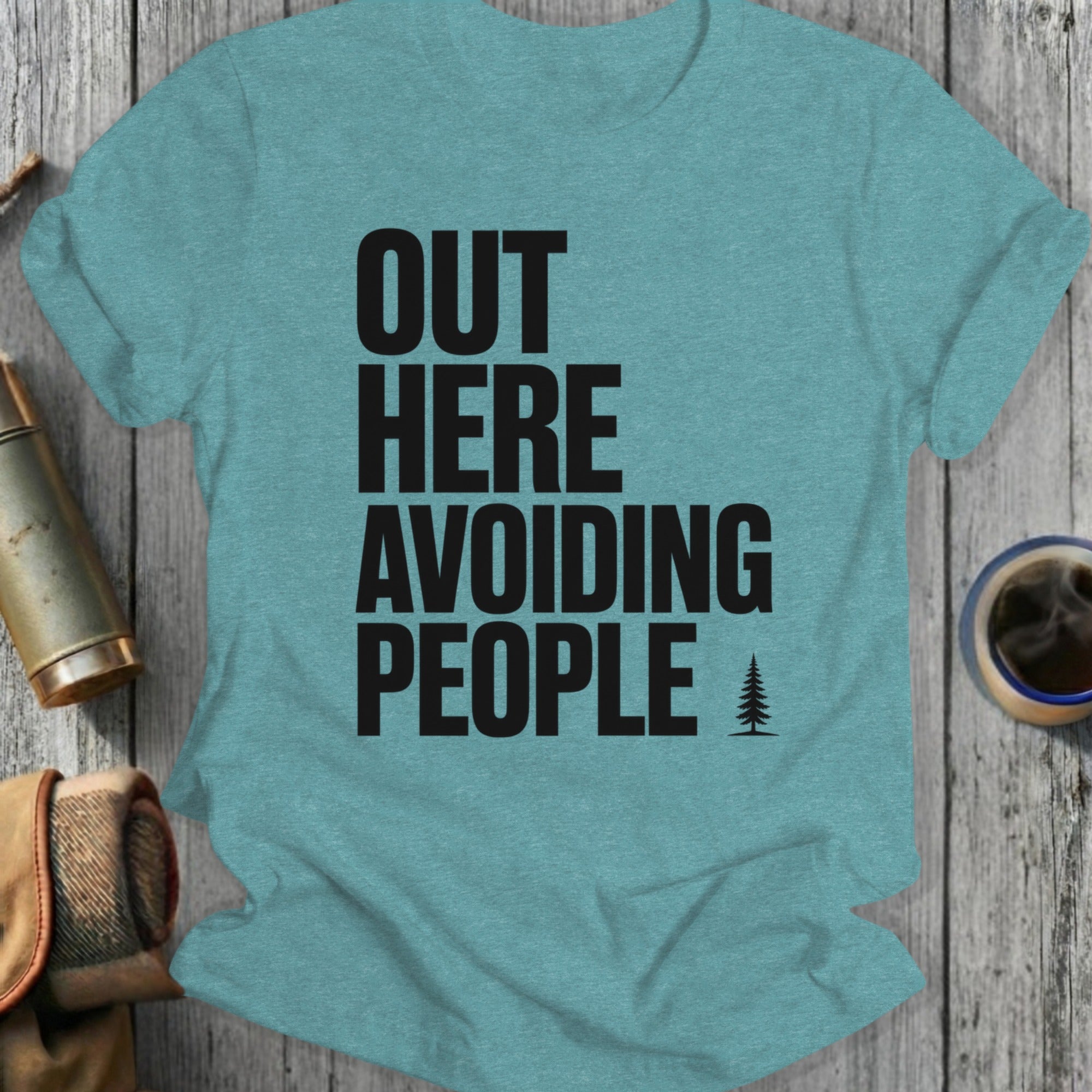 Teal t-shirt with black text "OUT HERE AVOIDING PEOPLE" and a small tree.