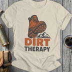 Cream t-shirt with graphic of boot, mountains, and text "DIRT THERAPY".