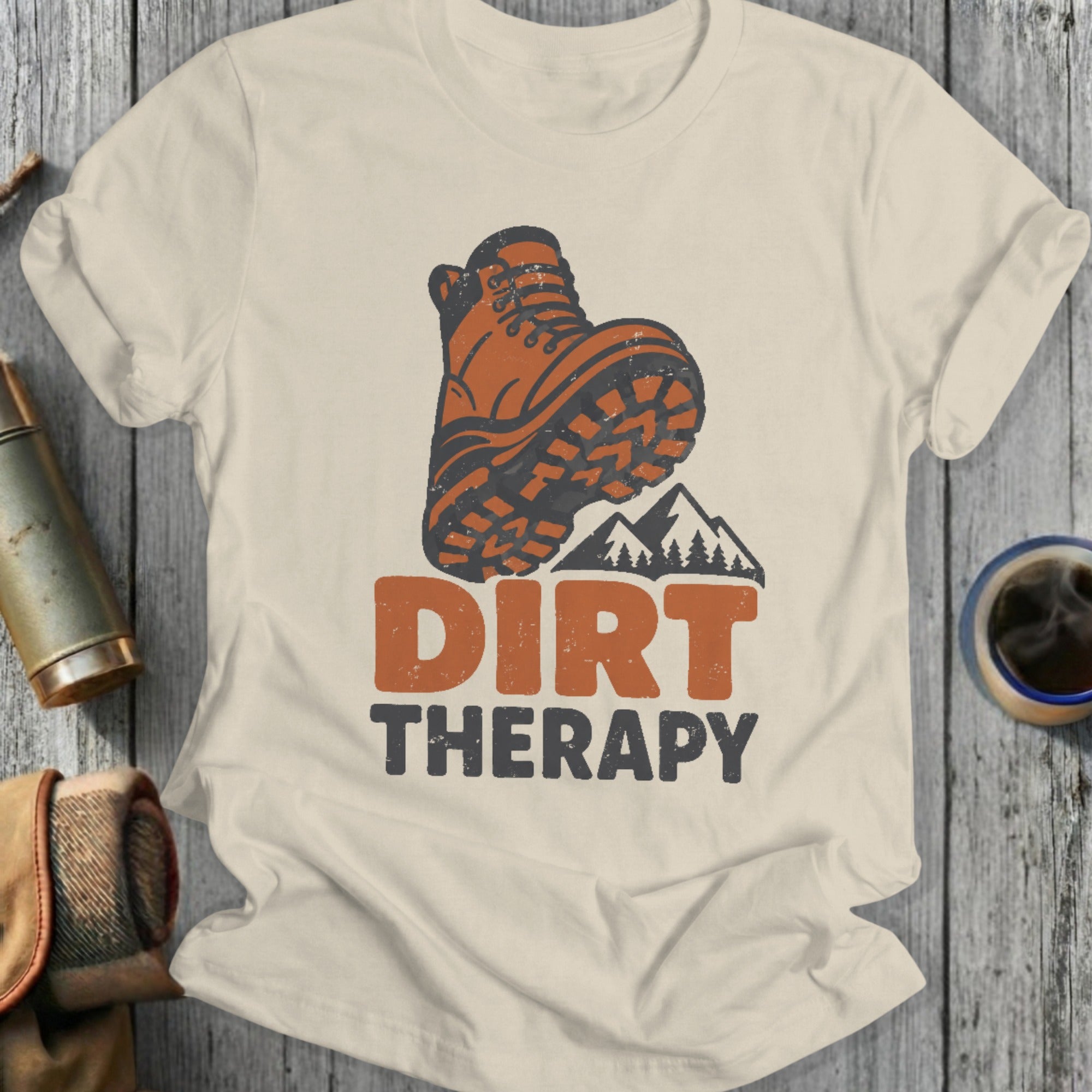 Cream t-shirt with graphic of boot, mountains, and text "DIRT THERAPY".