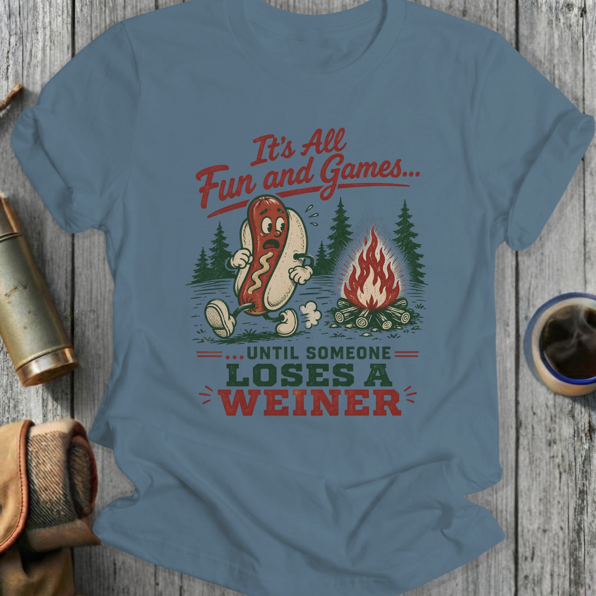 T-shirt graphic of a hot dog at a campfire with text, "It's All Fun and Games... Until Someone Loses a Weiner."