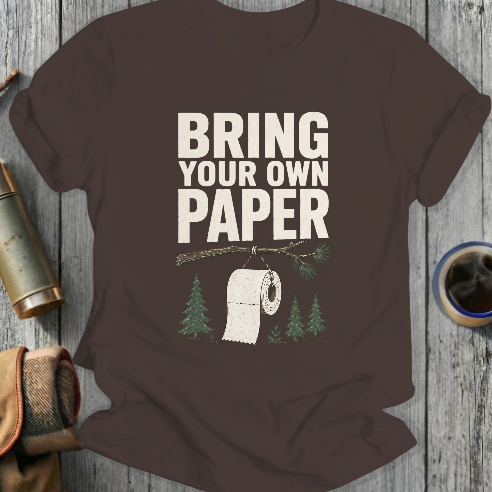 Brown t-shirt with "Bring Your Own Paper" text and toilet paper on a tree branch.