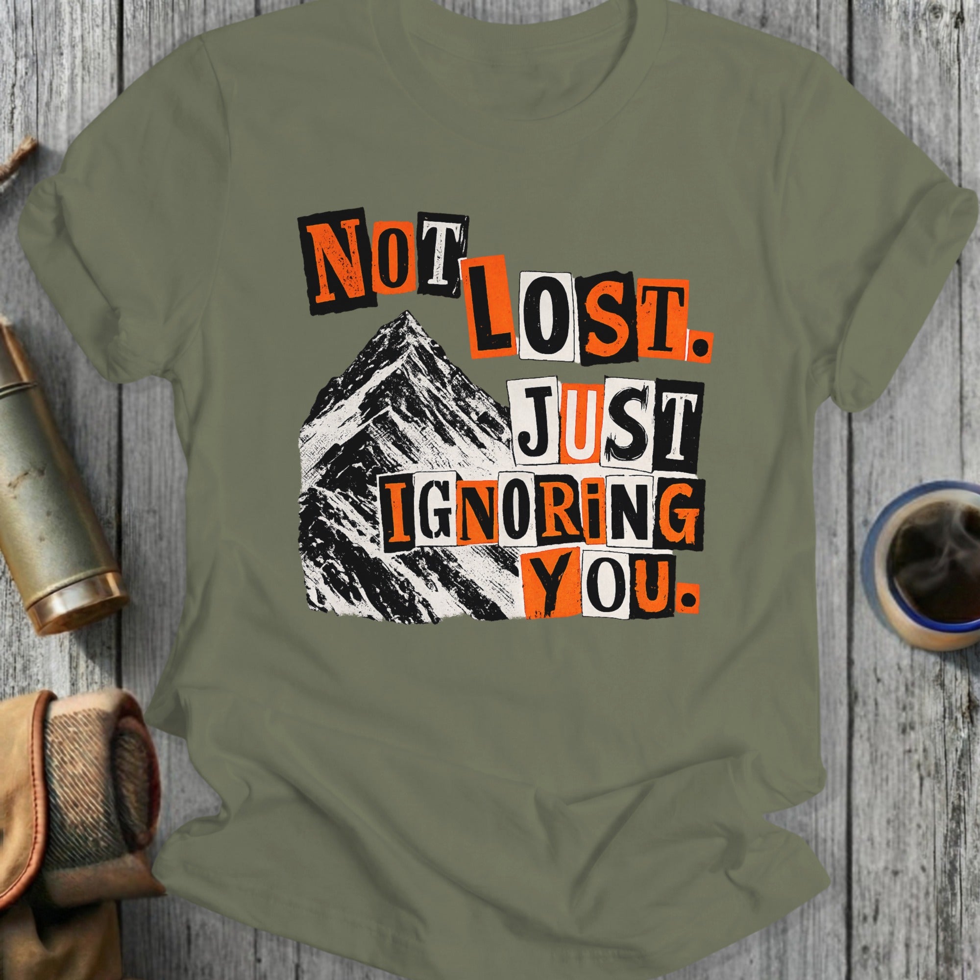 Olive green t-shirt with "Not Lost. Just Ignoring You." text and mountain graphic.