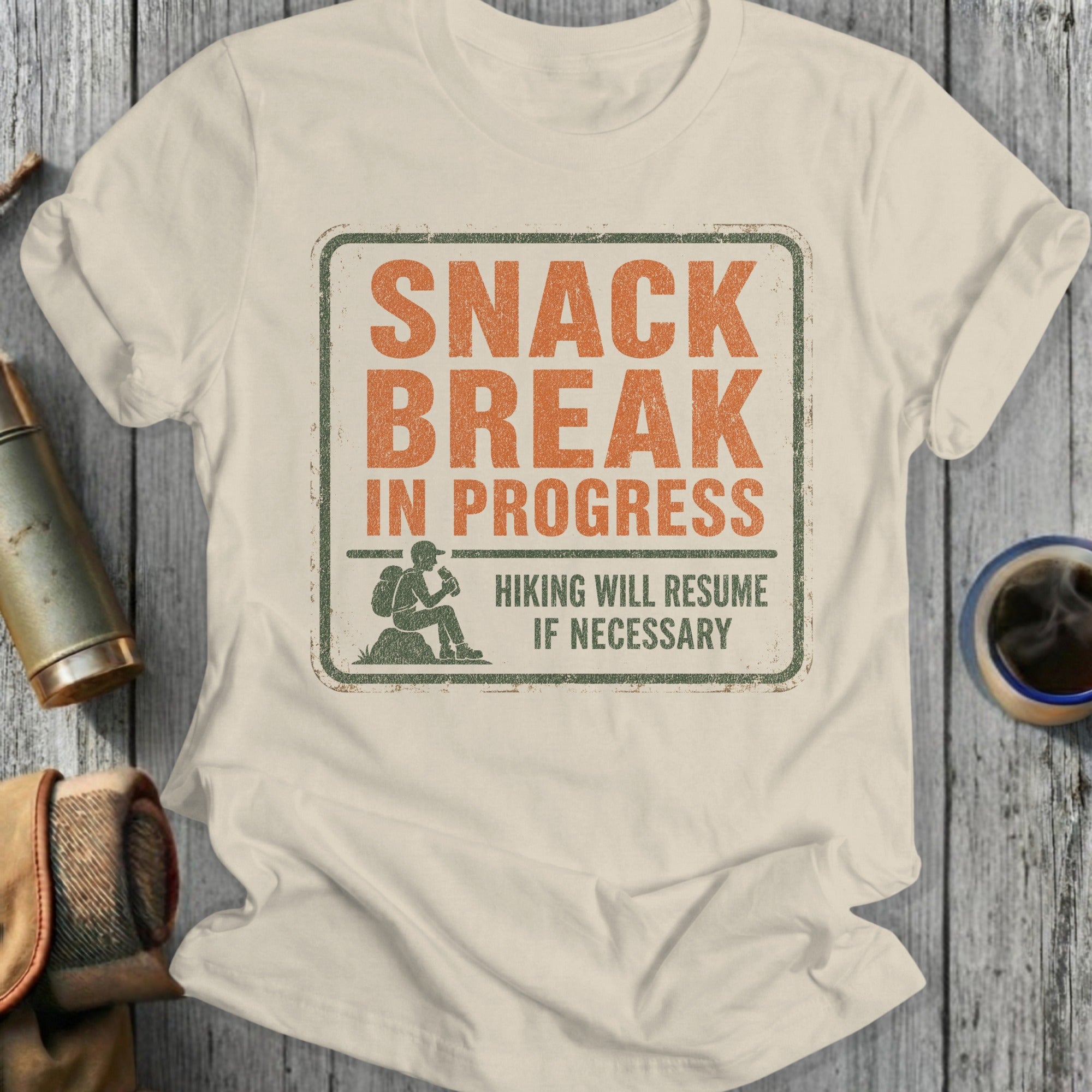 Light cream t-shirt with distressed graphic of a hiker and text "SNACK BREAK IN PROGRESS".