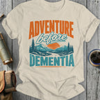 Cream t-shirt with "ADVENTURE before DEMENTIA" text and mountain landscape design.