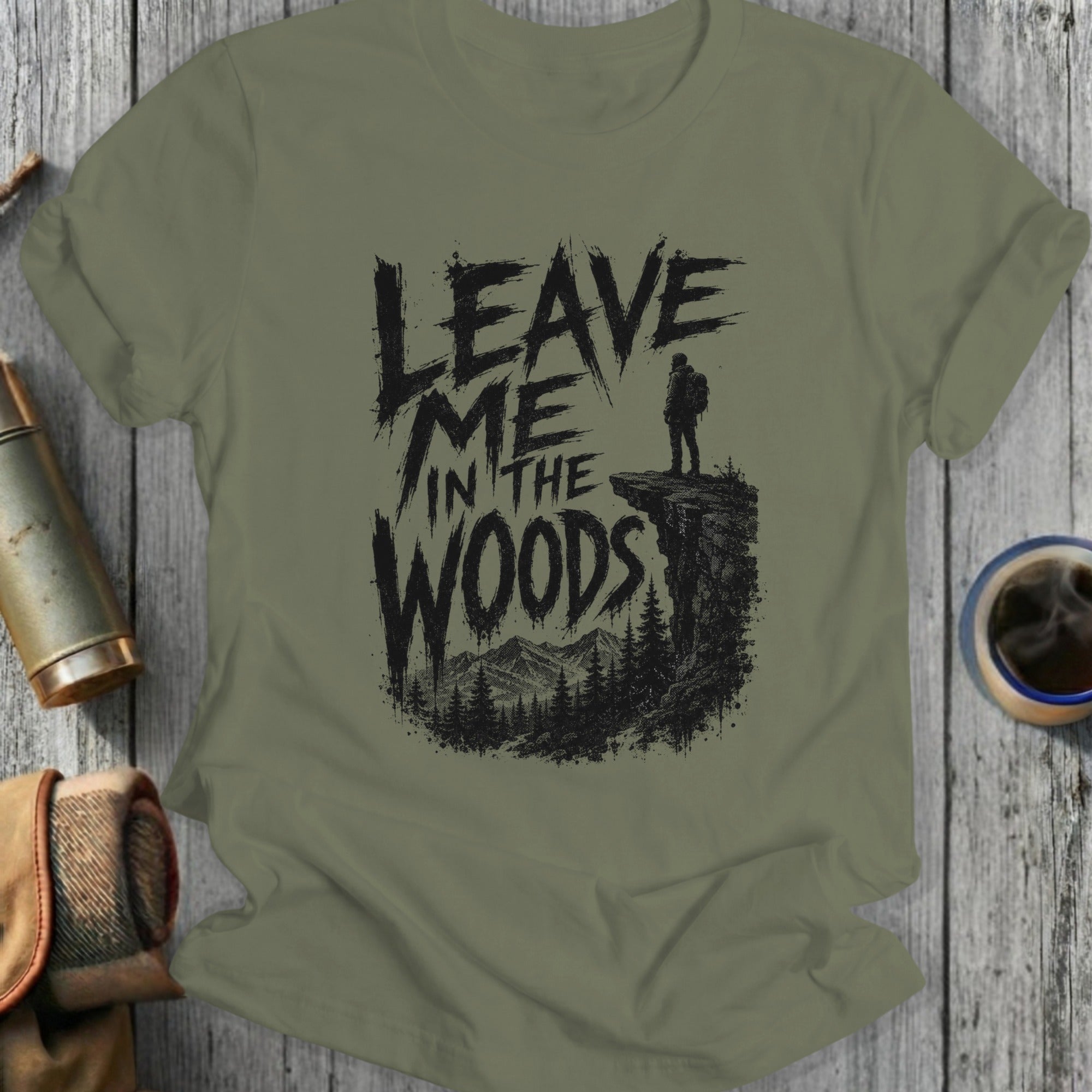 Olive green t-shirt with "Leave Me in the Woods" text and a hiker on a cliff.