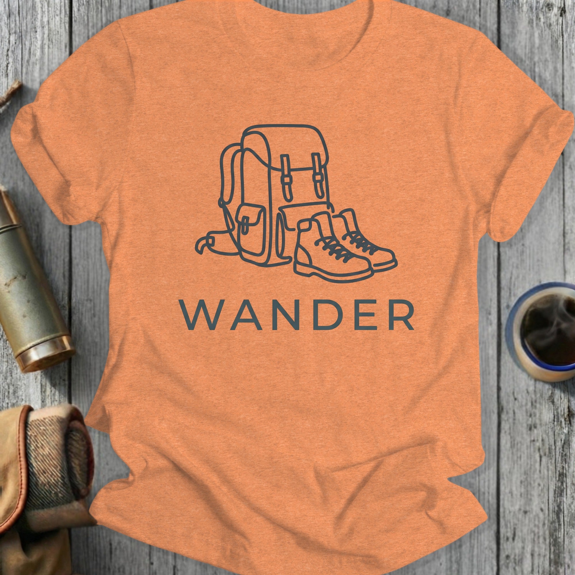 Orange t-shirt with line art of a backpack and hiking boots, and the word "WANDER".