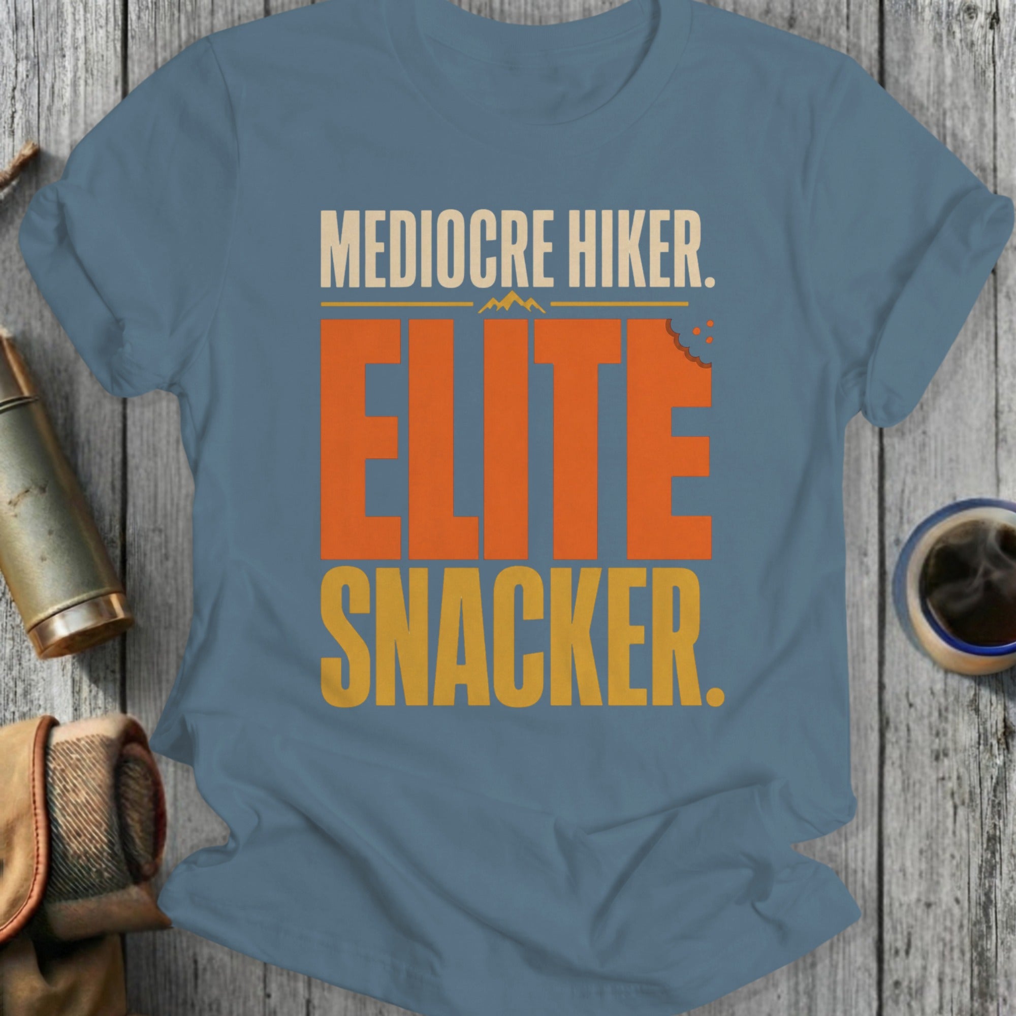 Mediocre Hiker. Elite Snacker. orange and yellow text on blue t-shirt.
