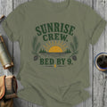 Olive green t-shirt with "SUNRISE CREW. BED BY 9." graphic.