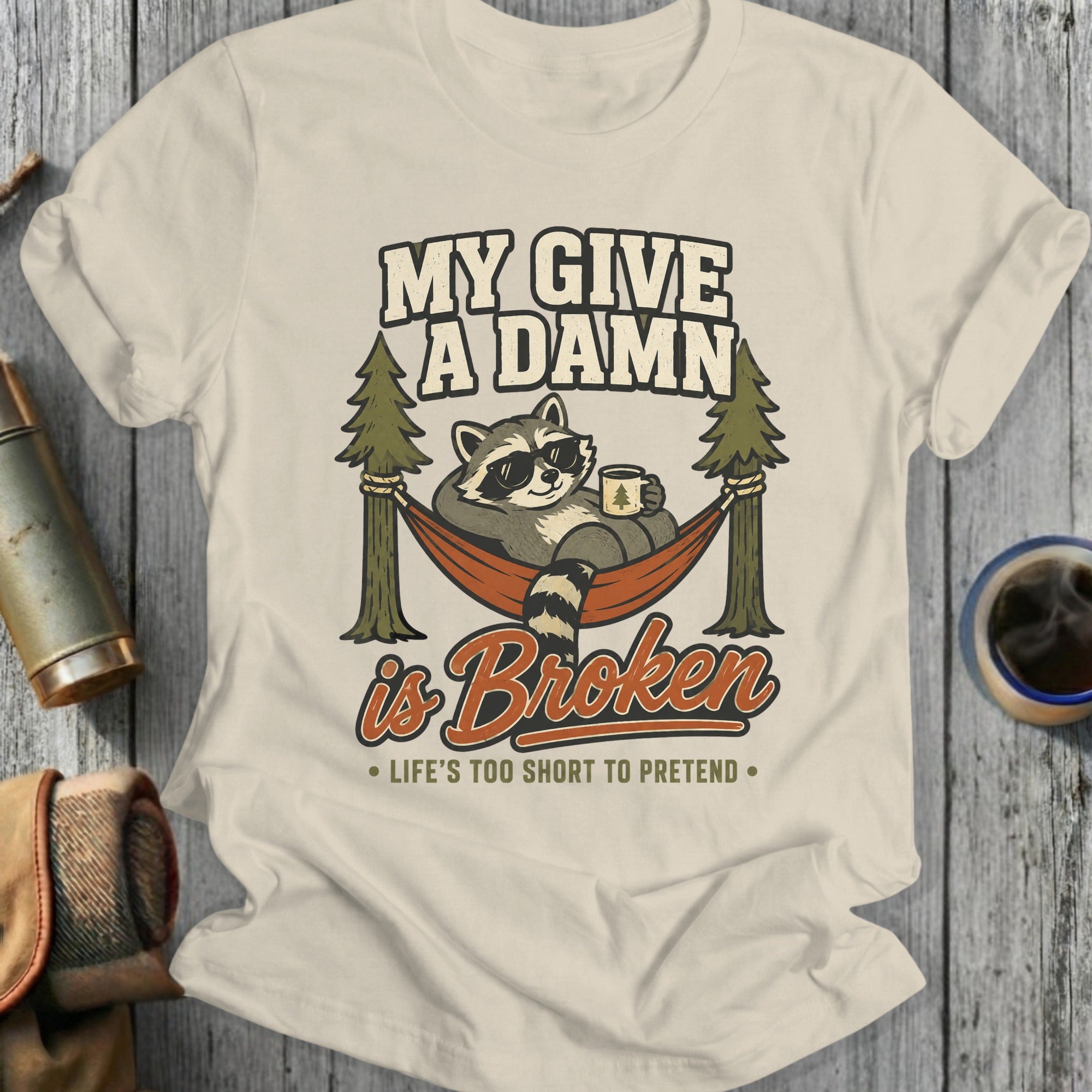 T-shirt graphic: raccoon in hammock with coffee, text "My Give A Damn is Broken".