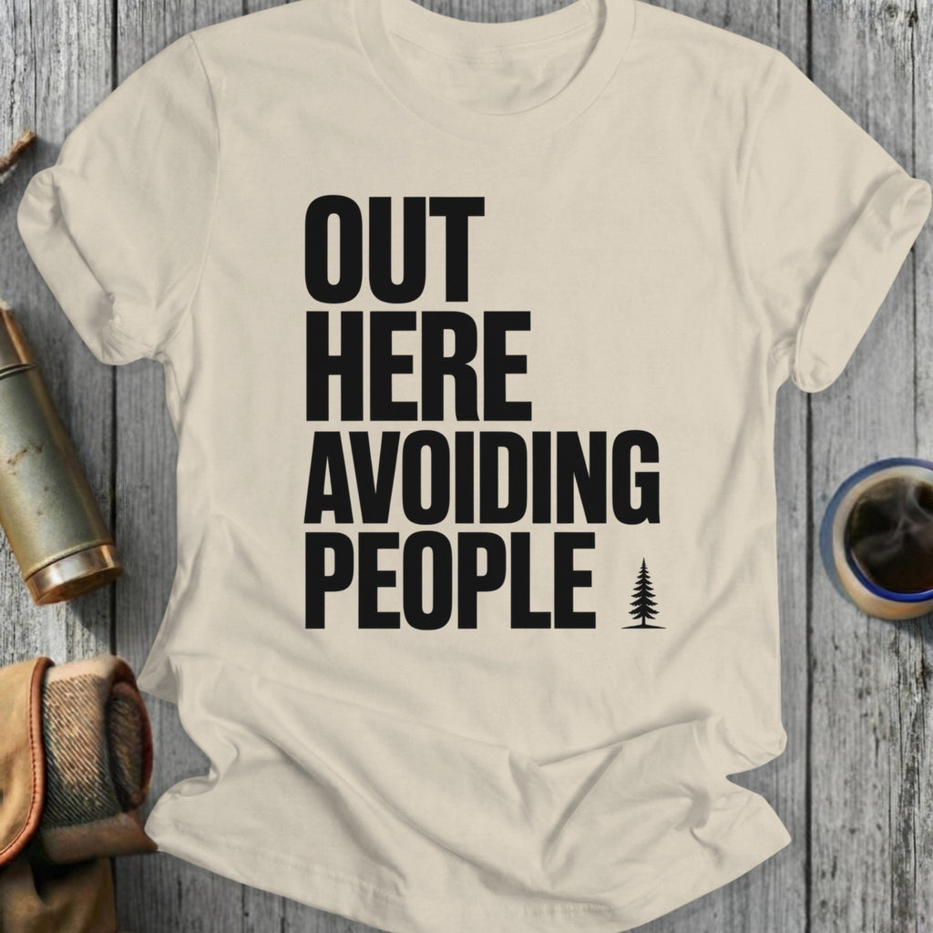 T-shirt with black text "OUT HERE AVOIDING PEOPLE" and a small tree graphic.